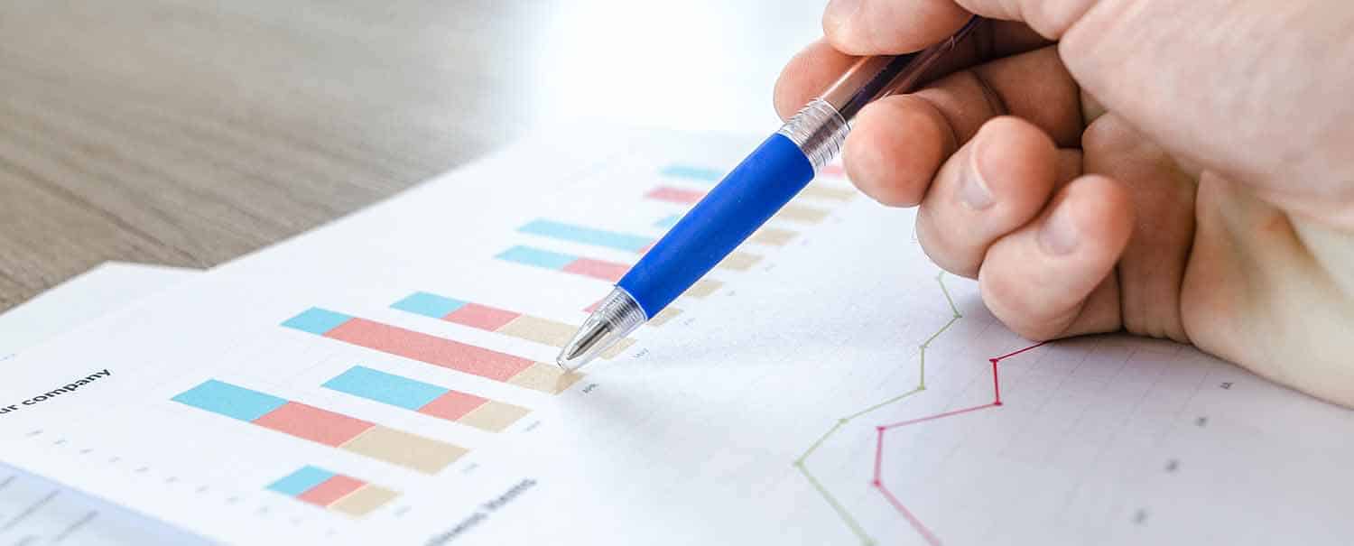 Hand mit Stift über Diagrammen und Auswertung